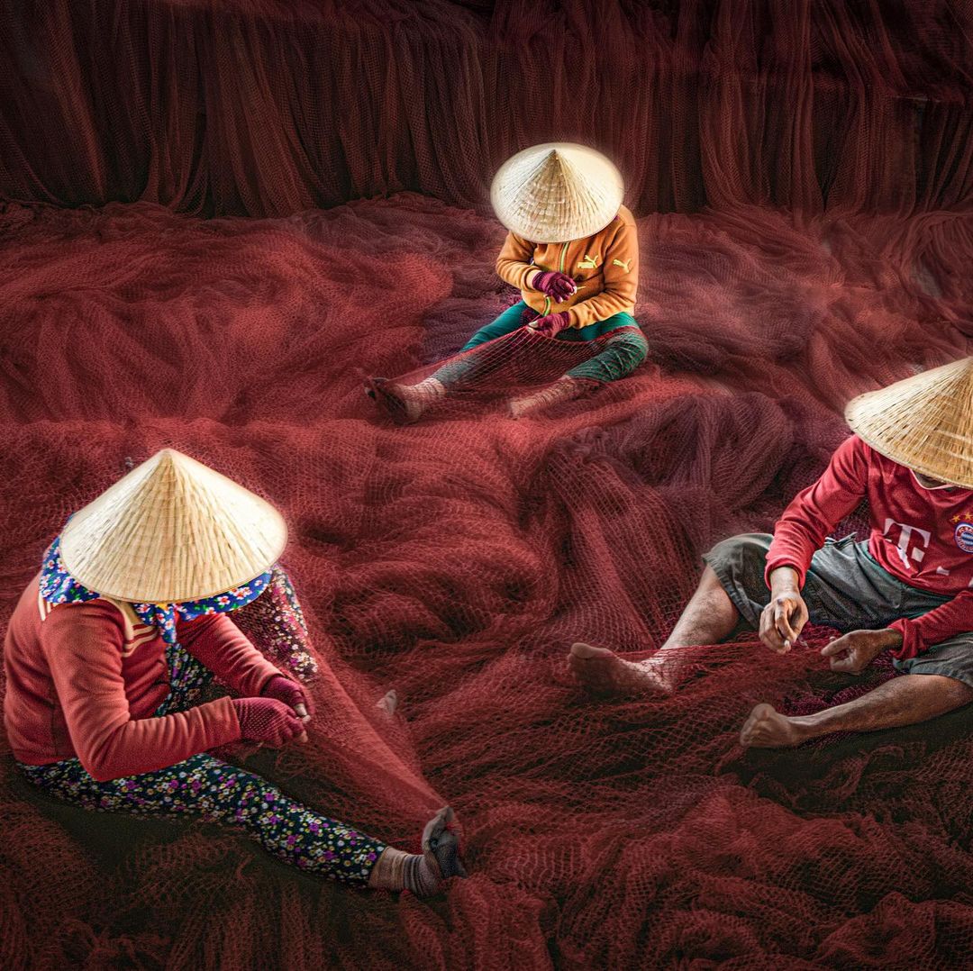 Red picture of three fishermen wearing native hat working on a fish net