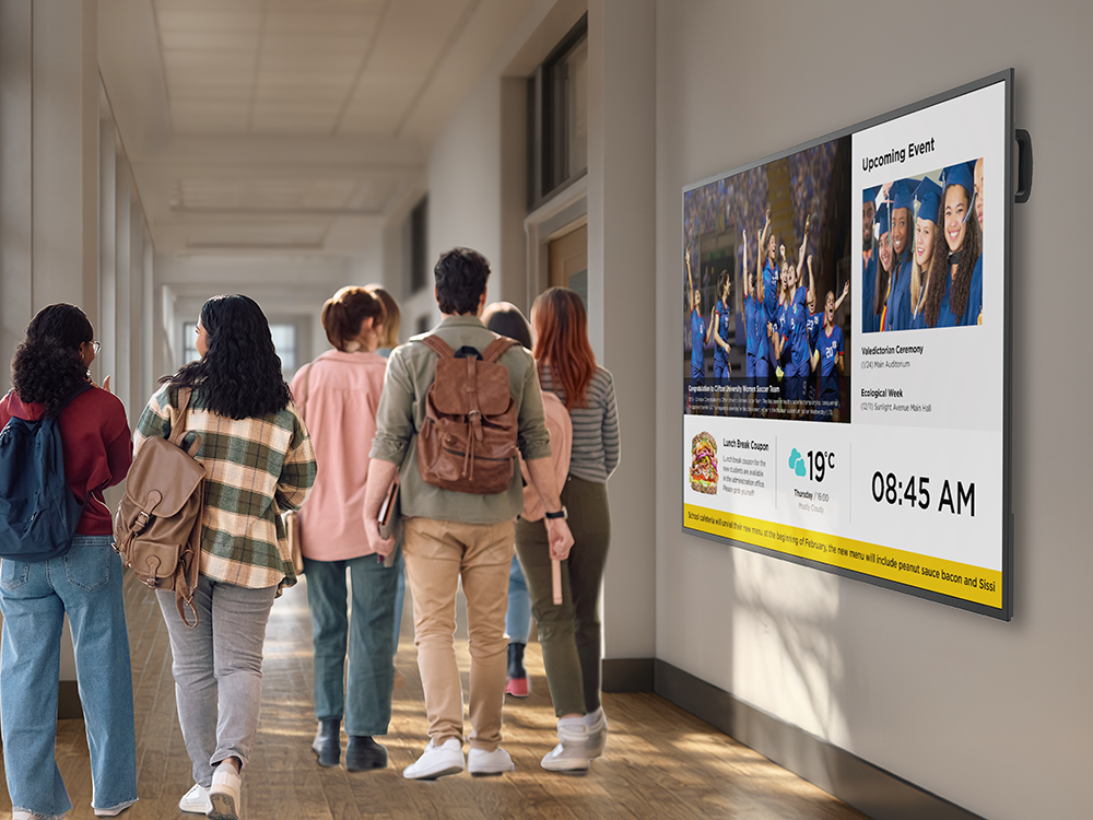 Students walking past a commercial digital signage display in a campus hallway